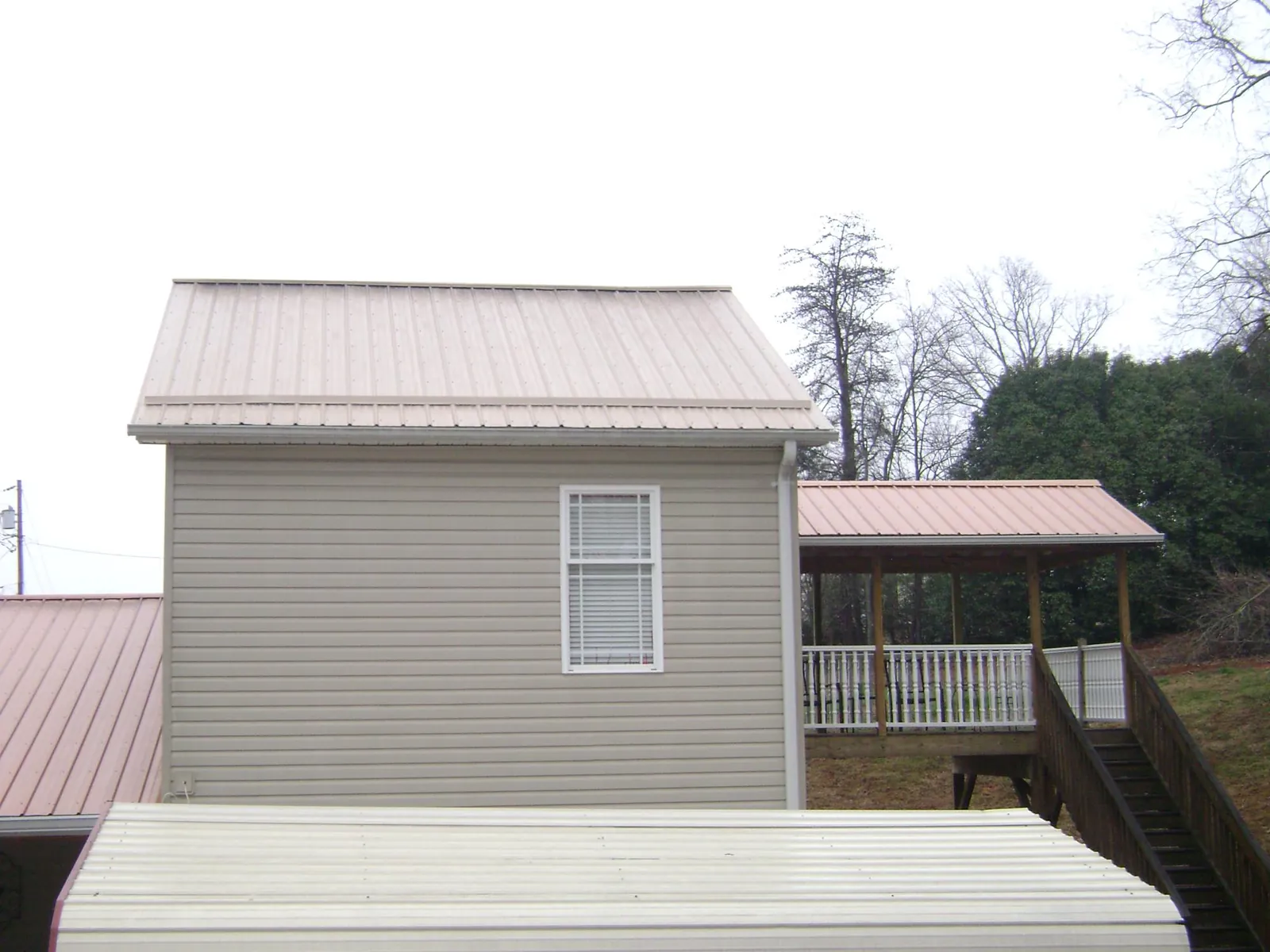 Tan metal roofs on a two story addition and attached porch, from a Roof Replacement job in Belleville